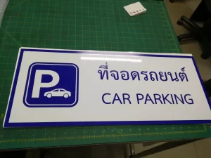 ป้ายที่จอดรถยนต์ CAR PARKING สองภาษาไทย-อังกฤษ อลูมิเนียมพื้นขาวกรอบน้ำเงิน โลโก้ตัว P พร้อมรูปรถยนต์ ถ่ายบนโต๊ะในโรงงาน