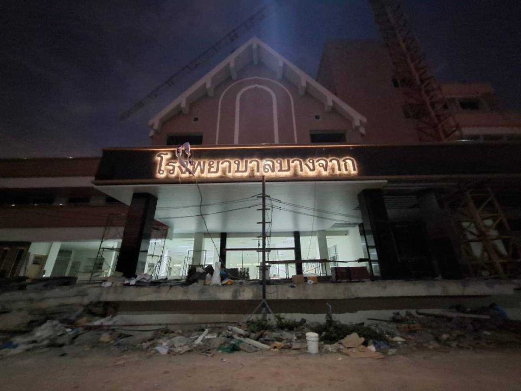 ป้ายชื่อโรงพยาบาลบางจาก ตัวอักษรสแตนเลสไฟ LED ส่องสว่างยามค่ำคืน มุมใกล้เห็นตัวอักษรเรืองแสง